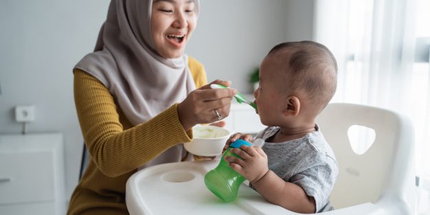 mother-feeding-her-baby-boy-while-sitting-high-chair_8595-12875 ways to introduce solid foods to your baby | BookDoc