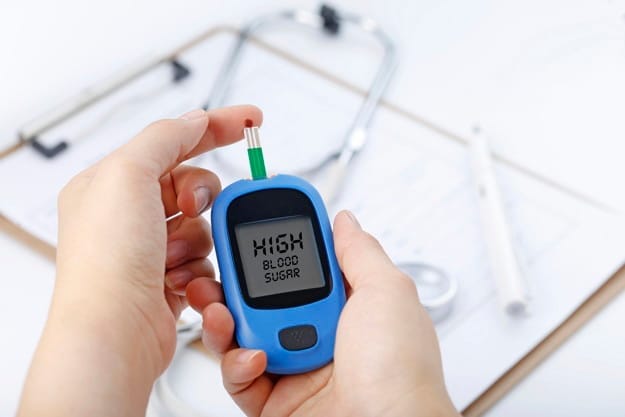 Hand holding a blood glucose meter measuring blood sugar, the background is a stethoscope and chart file taking measurement for blood glucose meter