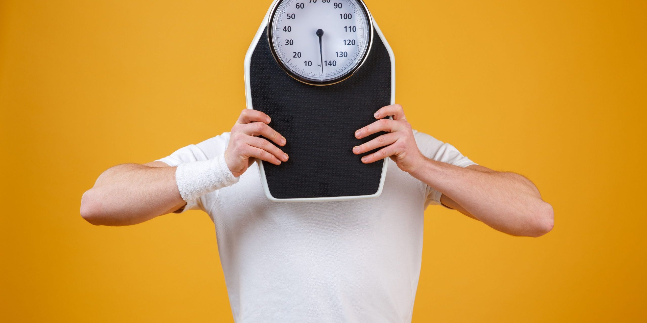 Young sports man hiding face behind weight scales Young sports man hiding face behind weight scales | BookDoc
