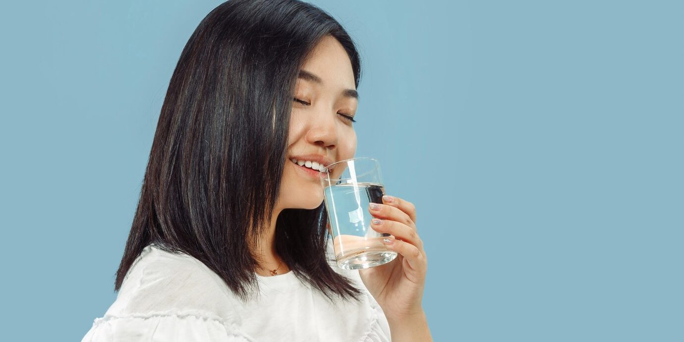 korean-young-woman-s-half-length-portrait-blue-space-female-model-white-shirt-enjoying-drinking-water_155003-26639