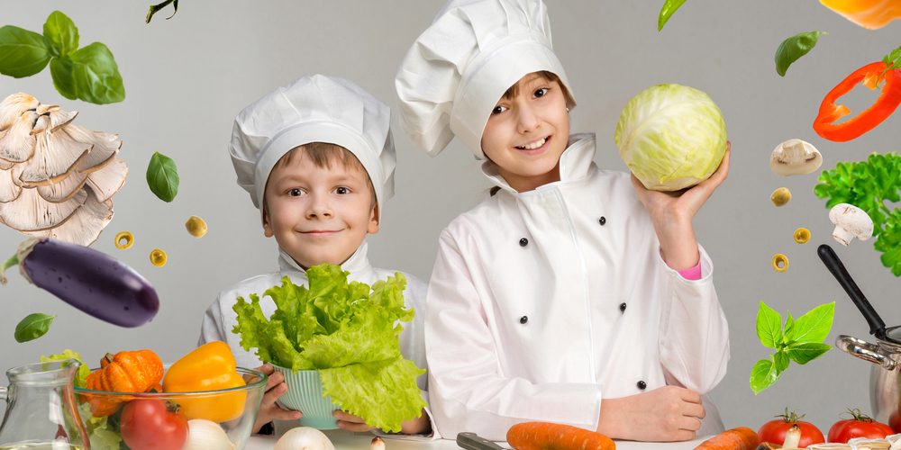 Two,Smiling,Children-cooks,By,The,Table,With,Flying,Vegetables,In