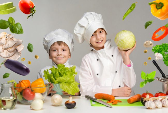 Two,Smiling,Children-cooks,By,The,Table,With,Flying,Vegetables,In