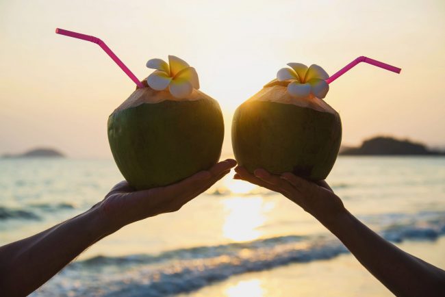 silhouette-fresh-coconut-couples-hands-with-plumeria-decorated-beach-with-sea-wave-tourist-with-fresh-fruit-sea-sand-sun-vacation-concept (1)